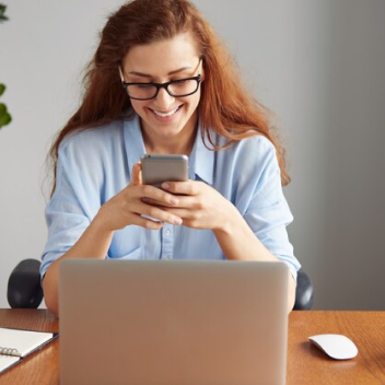 mulher usando  celulcar em frente ao notebook